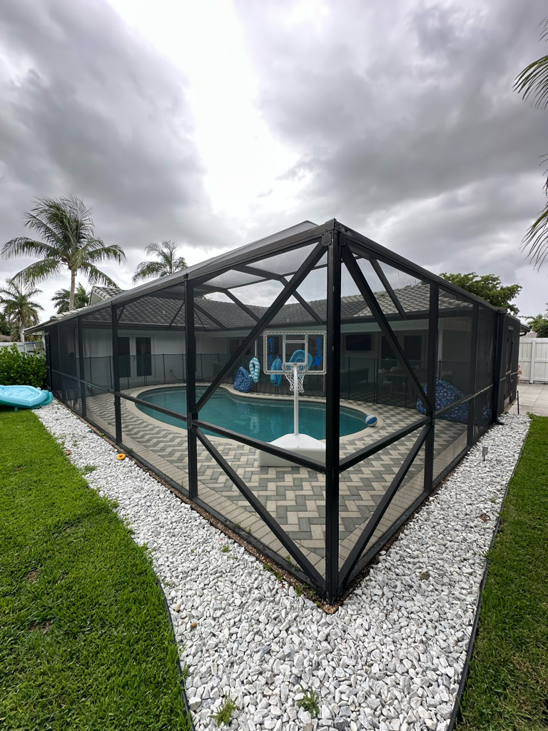 Large pool screen enclosure exterior with dark aluminum frame and decorative pavers