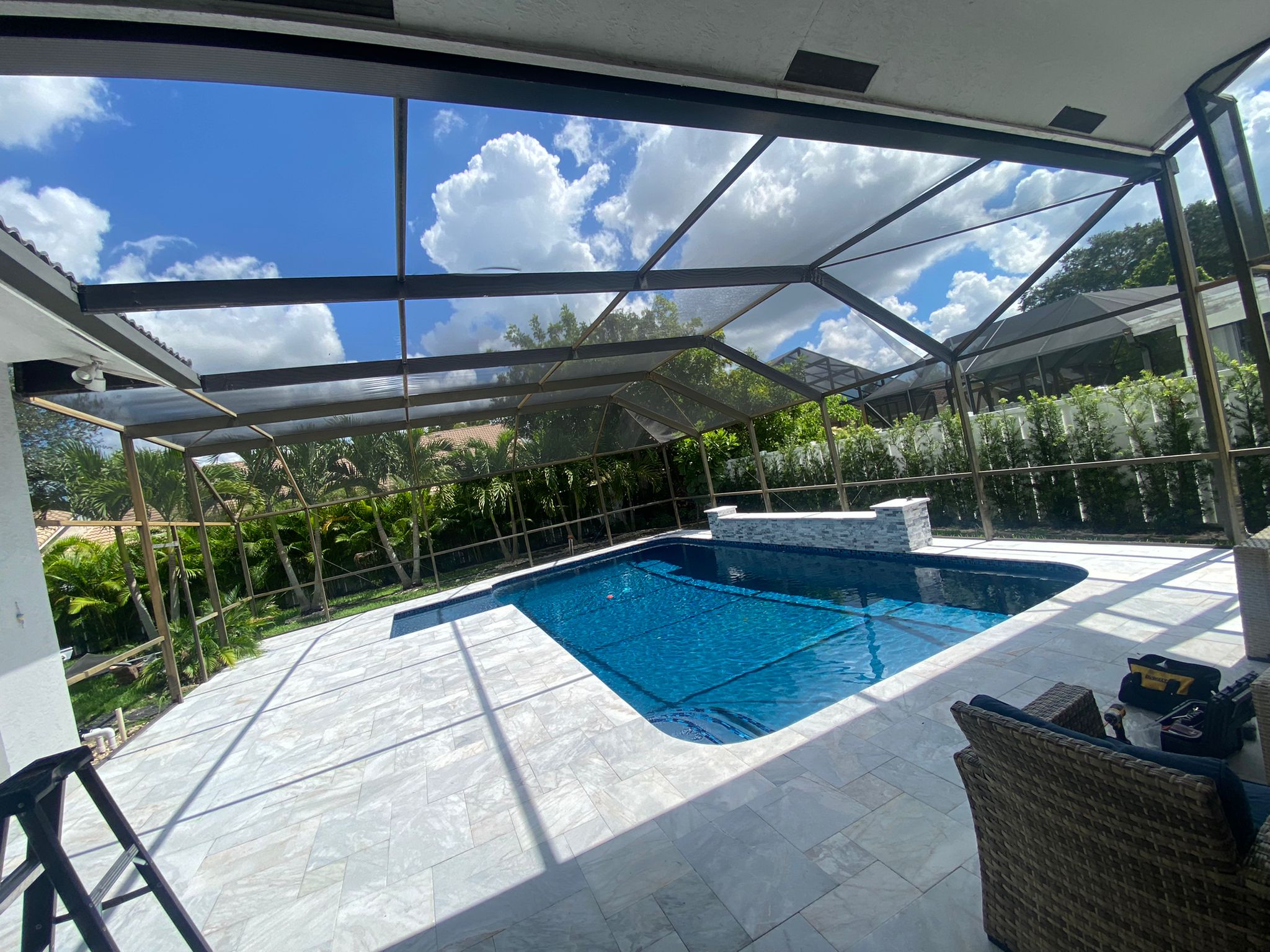 Luxury pool screen enclosure interior with blue pool, travertine deck, and tropical landscaping