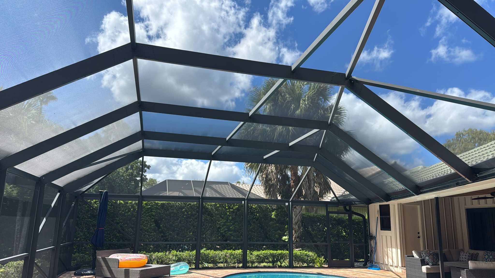 Inside pool screen enclosure looking up at dark screen panels against blue sky with palm tree