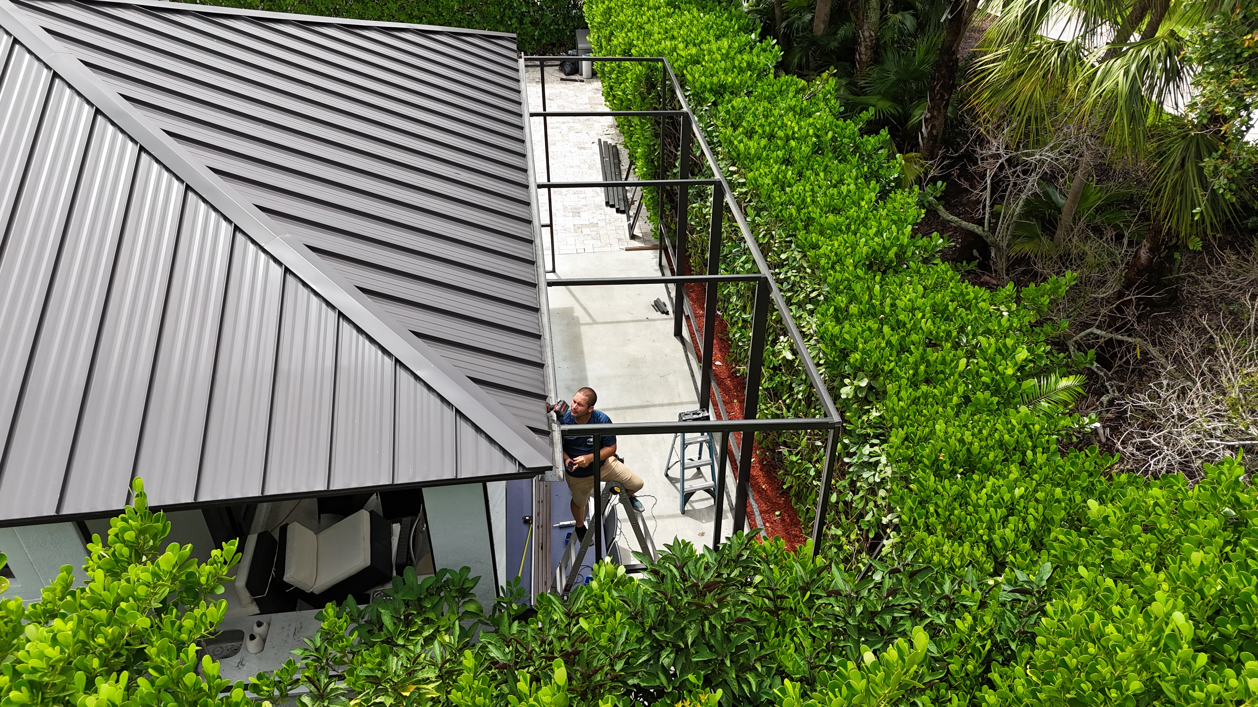 Aerial drone view of screen room construction in progress — team member on ladder at luxury home