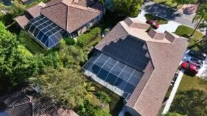 Aerial view of Florida residential homes with pool enclosures and tiled roofs, showcasing a modern architectural design with lush greenery.